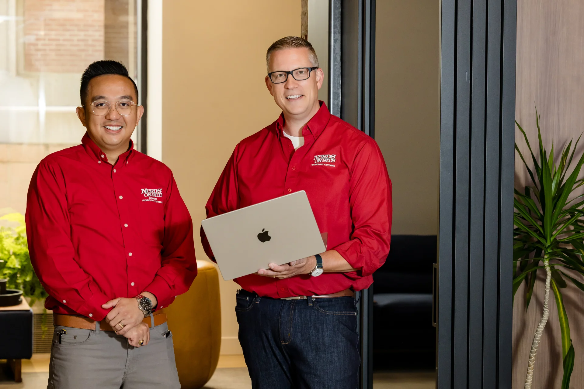 Two Nerds On Site technicians in branded red shirts collaborating with a laptop