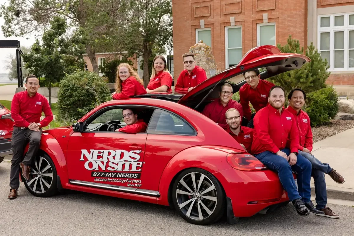 Nerds On Site team posing with the iconic branded red VW Beetle